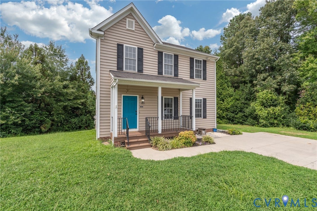 Two-story residential structure with light-colored siding, contrasting dark shutters, and a covered front porch featuring a vibrant blue entry door