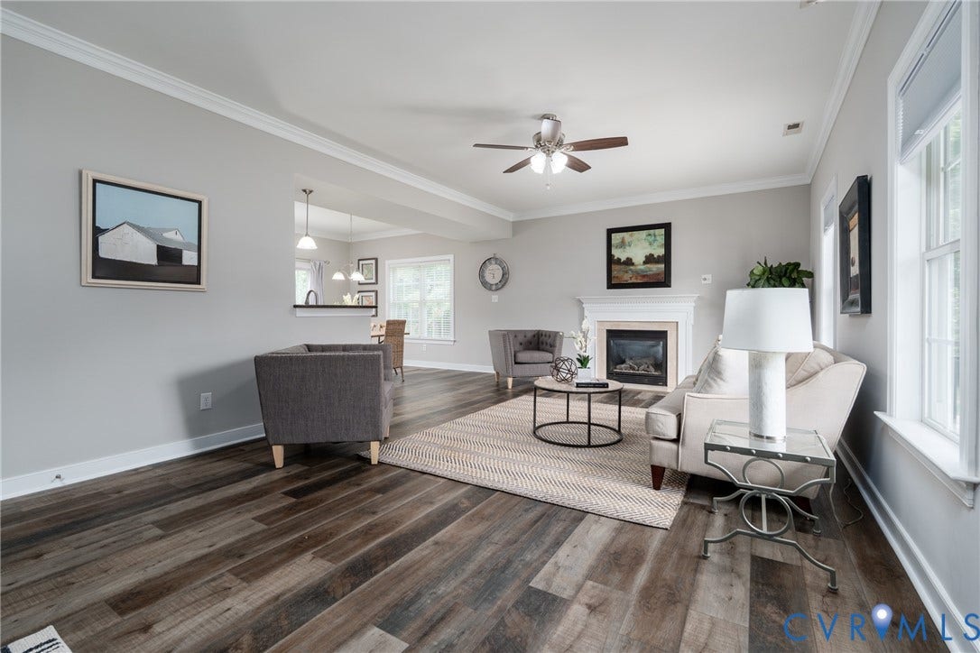 Crown molding, wood-finish flooring, fireplace, ceiling fan, and multiple windows