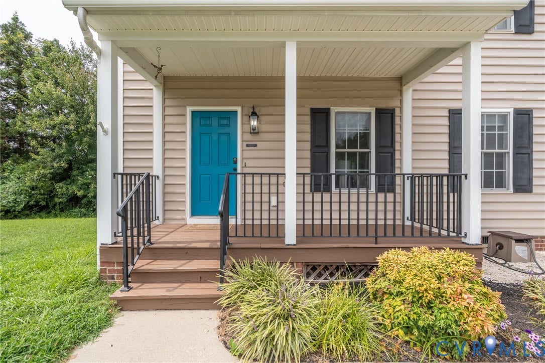 Covered front porch with wood-finish decking, black metal railings, and a vibrant blue entry door