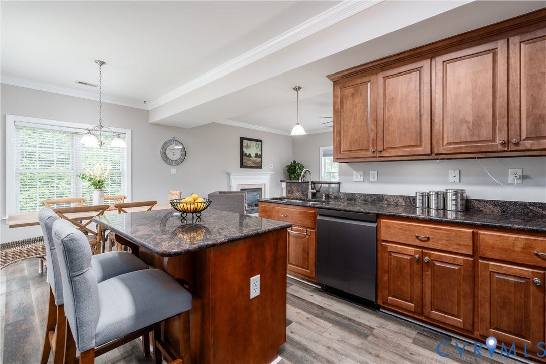 Kitchen island with seating, wood-finish flooring, dark stone countertops, wood cabinetry, and a stainless steel sink