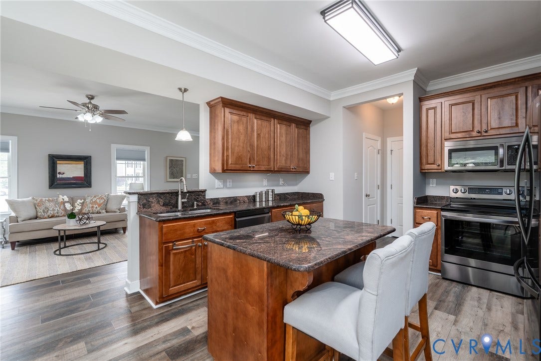 Kitchen featuring wood-finish flooring, dark wood cabinetry, stainless steel appliances, and a central island with a stone countertop
