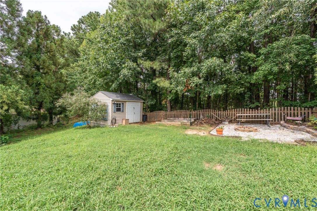 Expansive backyard with a storage shed, wood picket fencing, and a gravel patio with a built-in fire pit