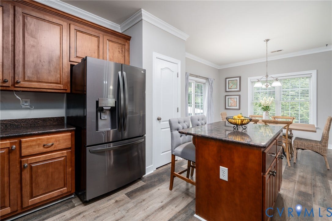 Kitchen featuring wood cabinetry, dark countertops, a central island with seating, and wood-finish flooring