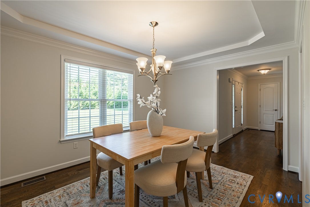 Tray ceiling with crown molding, hardwood flooring, and a multi-pane window
