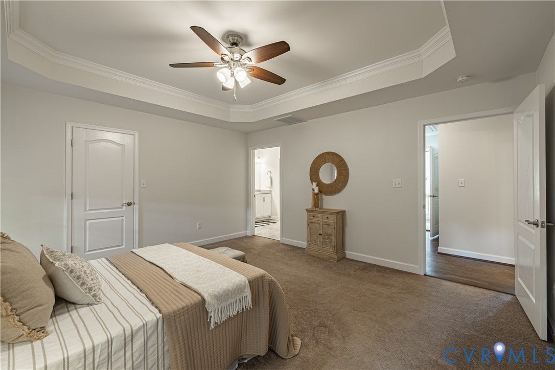 Tray ceiling with crown molding, ceiling fan with light fixture, carpeted flooring, and white paneled doors