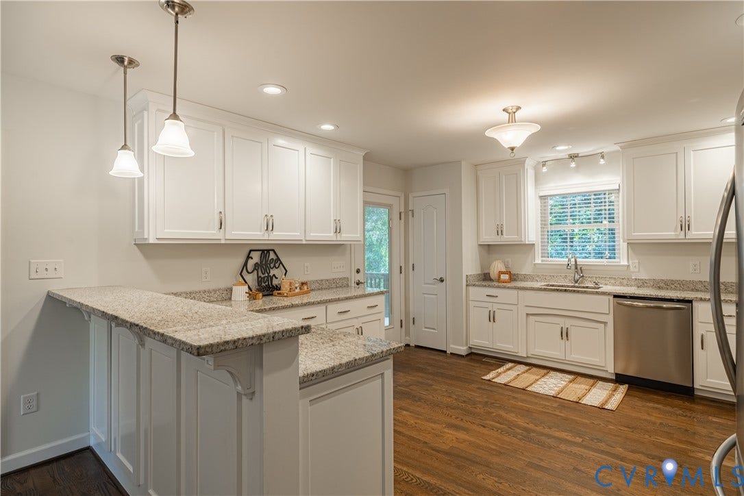 White shaker cabinetry, granite countertops, wood-finish flooring, stainless steel appliances, and pendant lighting