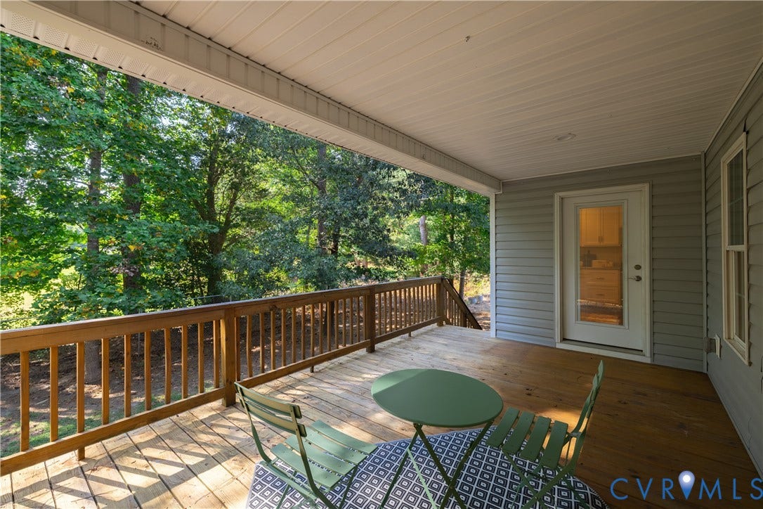 Covered wood deck with wood railing, light gray siding, and a white exterior door with glass insert