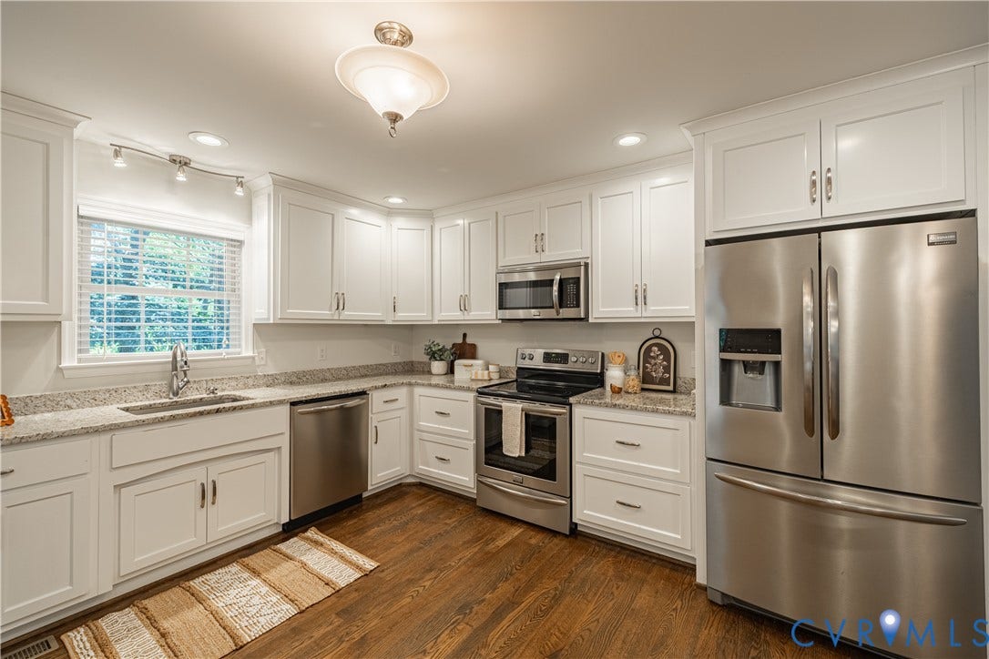 White shaker-style cabinetry, granite countertops, stainless steel appliances, wood-finish flooring, and recessed lighting
