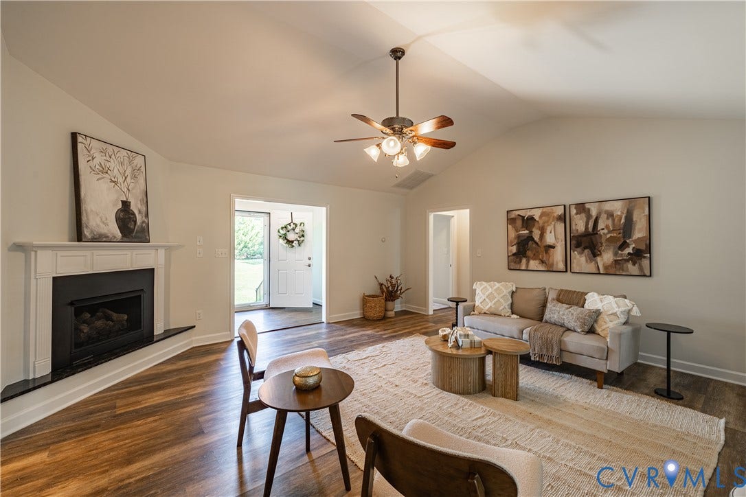 Vaulted ceiling, wood-finish flooring, built-in fireplace with white mantel, ceiling fan with integrated lighting, and a white paneled door
