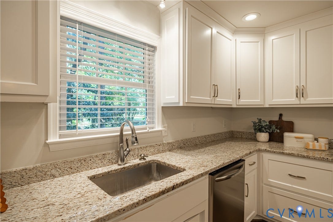 White shaker-style cabinetry with brushed nickel hardware, granite countertops, undermount stainless steel sink with a gooseneck faucet, and a stainless steel dishwasher