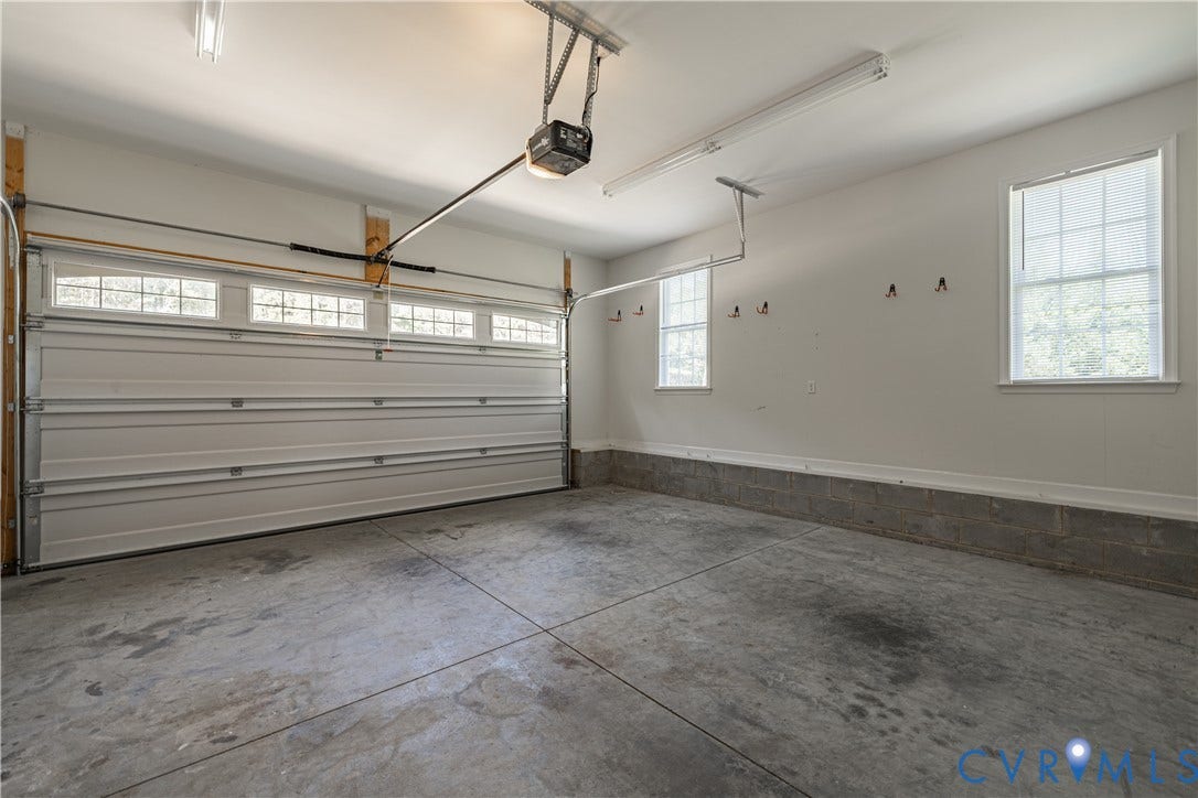 Concrete flooring, two windows, two overhead fluorescent light fixtures, and a roll-up garage door with transom-style windows