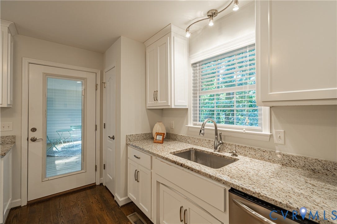 White shaker cabinetry, stainless steel sink, expansive countertop, wood-finish flooring, and a glass-paneled door