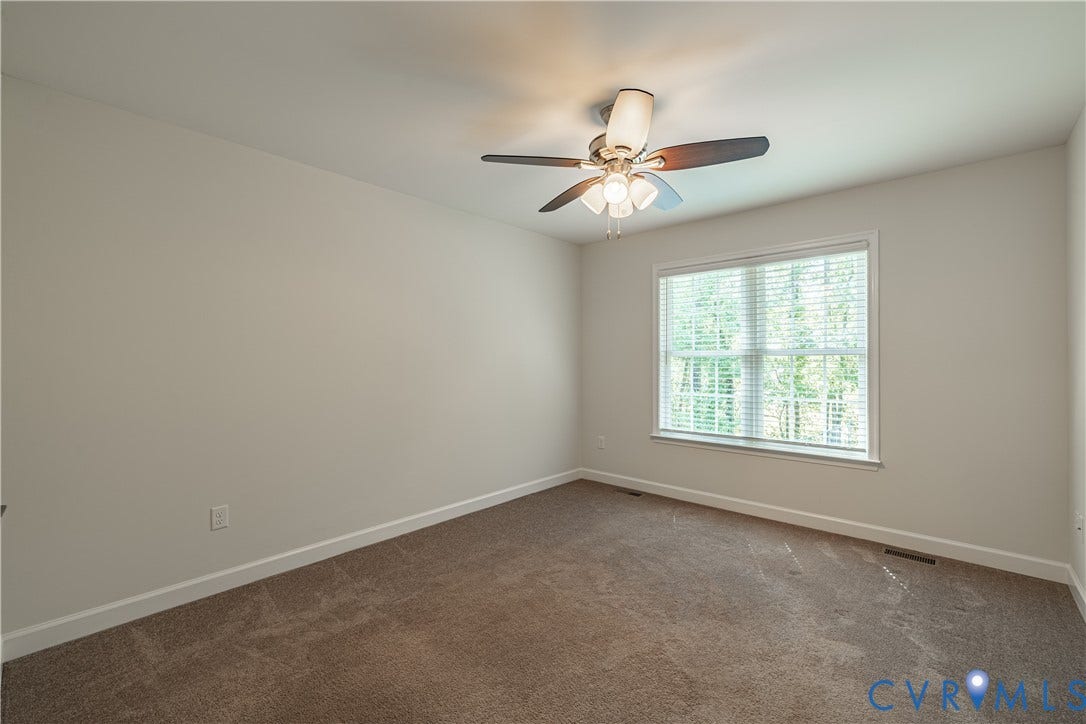 Neutral tone wall paint, textured carpeting, large window with blinds, and a ceiling fan with integrated lighting