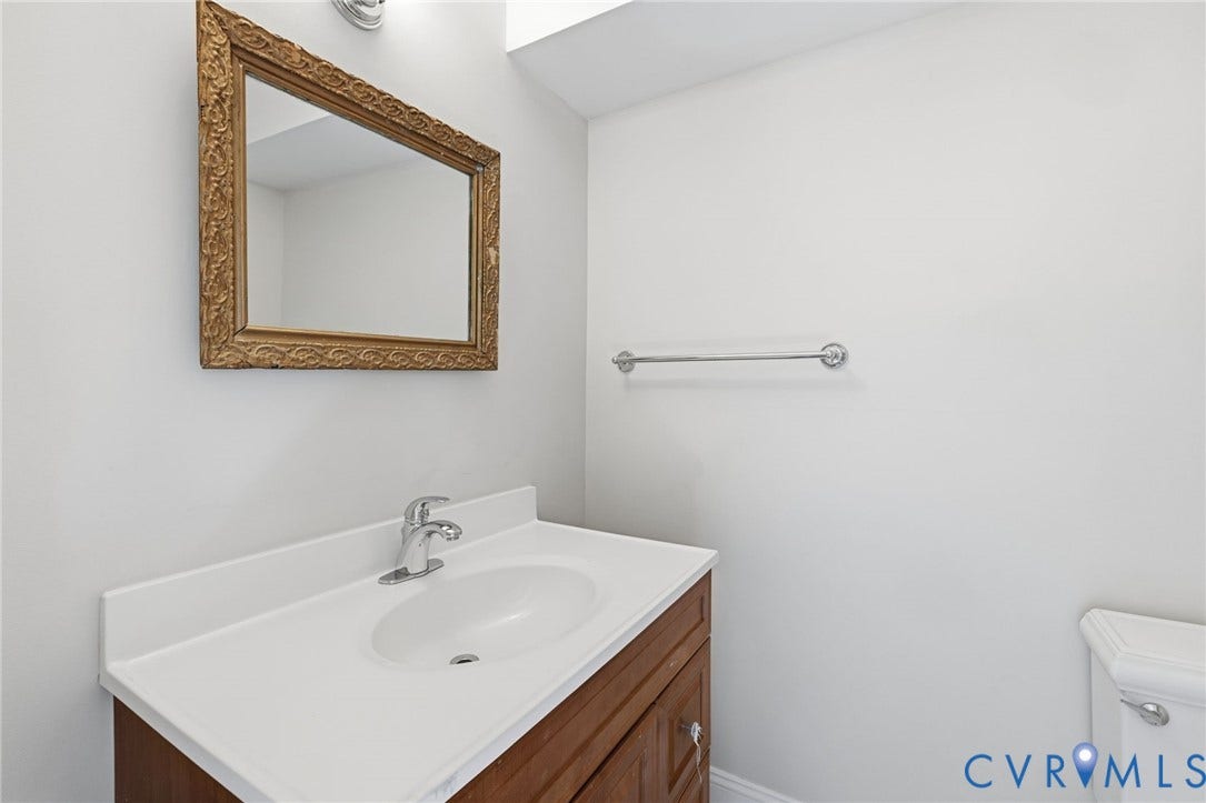 Wood-finish vanity with a white countertop and integrated sink, complemented by a decorative framed mirror and chrome faucet