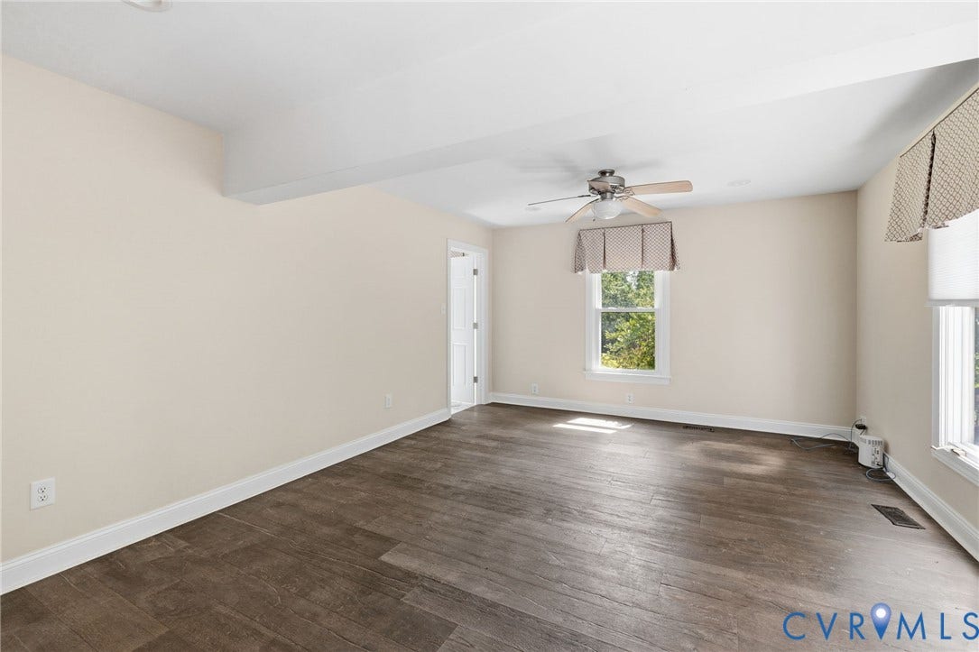Spacious room featuring wood-finish flooring, light-colored walls, multiple windows, and a ceiling fan