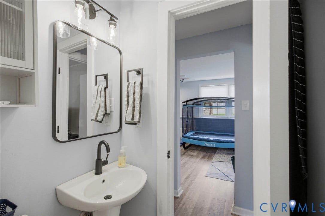 1905 Reagan Road, Henrico, VA 23228 Pedestal sink with a matte black faucet, framed vanity mirror, wall-mounted light fixture, and built-in cabinet storage