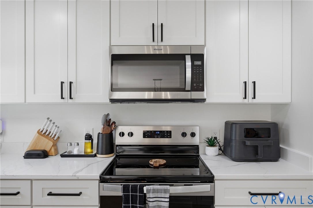 1905 Reagan Road, Henrico, VA 23228 White shaker-style cabinetry with matte black hardware, stainless steel over-the-range microwave, electric range, and light-toned countertops