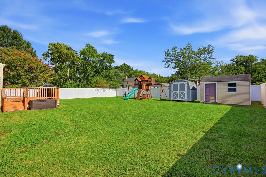 1905 Reagan Road, Henrico, VA 23228 Expansive grassy yard with a white privacy fence, wood-toned deck, and two detached storage sheds