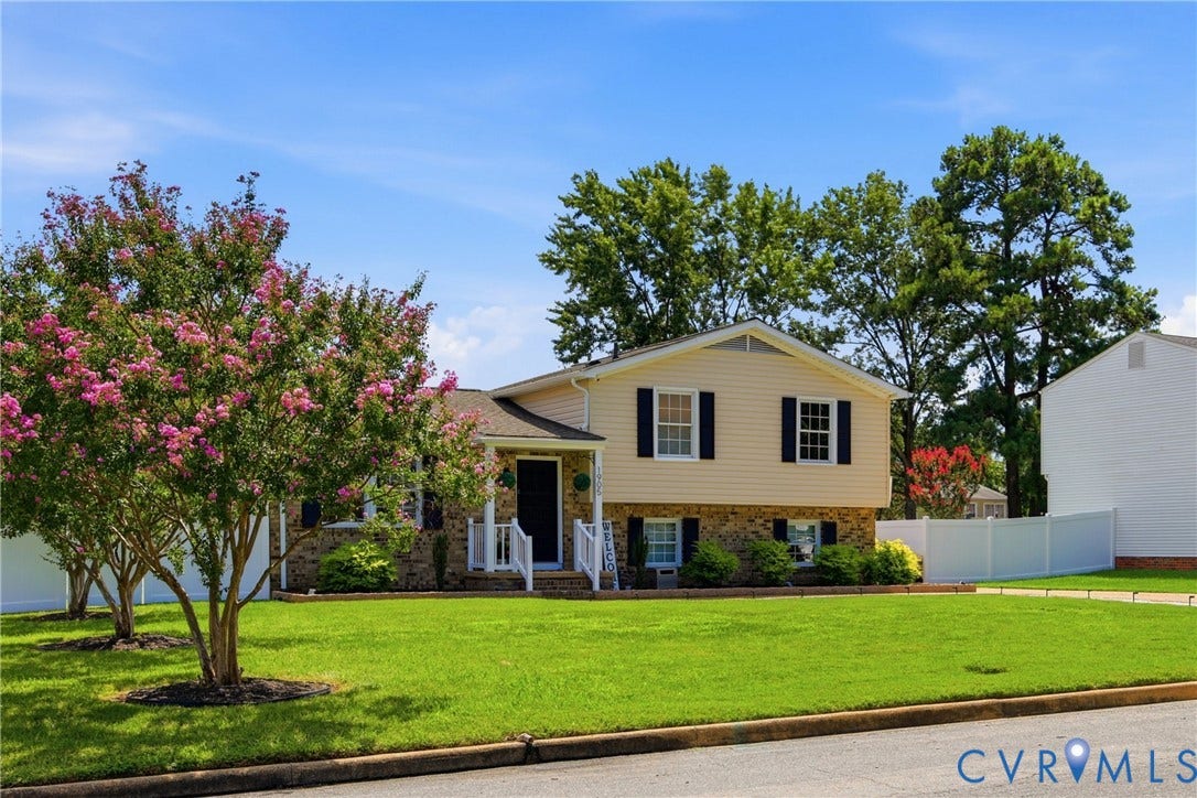 1905 Reagan Road, Henrico, VA 23228 Split-level residence featuring a stone and siding exterior, front lawn, mature flowering trees, and a white picket fence