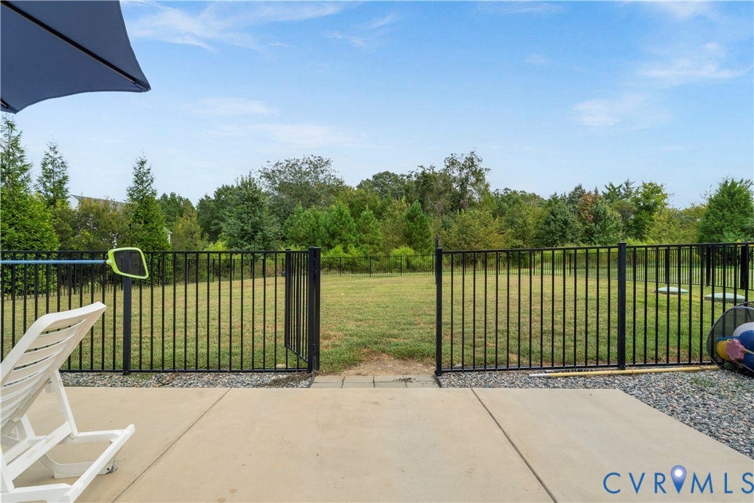 11707 Amara Drive, Chester / Highlands Golf Club, Chesterfield, VA 23838 Expansive patio with concrete slab and gravel border, featuring a black metal fence with a double gate opening to a grassy area