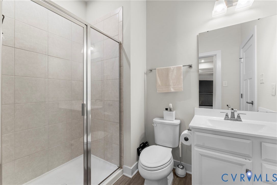 11707 Amara Drive, Chester / Highlands Golf Club, Chesterfield, VA 23838 Shower enclosure with glass door, tiled shower surround, single vanity with integrated sink, chrome faucet, and wood-finish flooring