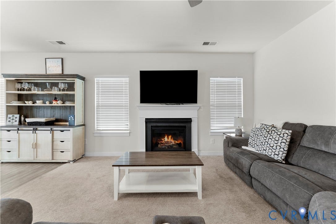 11707 Amara Drive, Chester / Highlands Golf Club, Chesterfield, VA 23838 Living area featuring a fireplace with a white mantel, two windows with blinds, and a built-in cabinetry unit with open shelving and lower storage