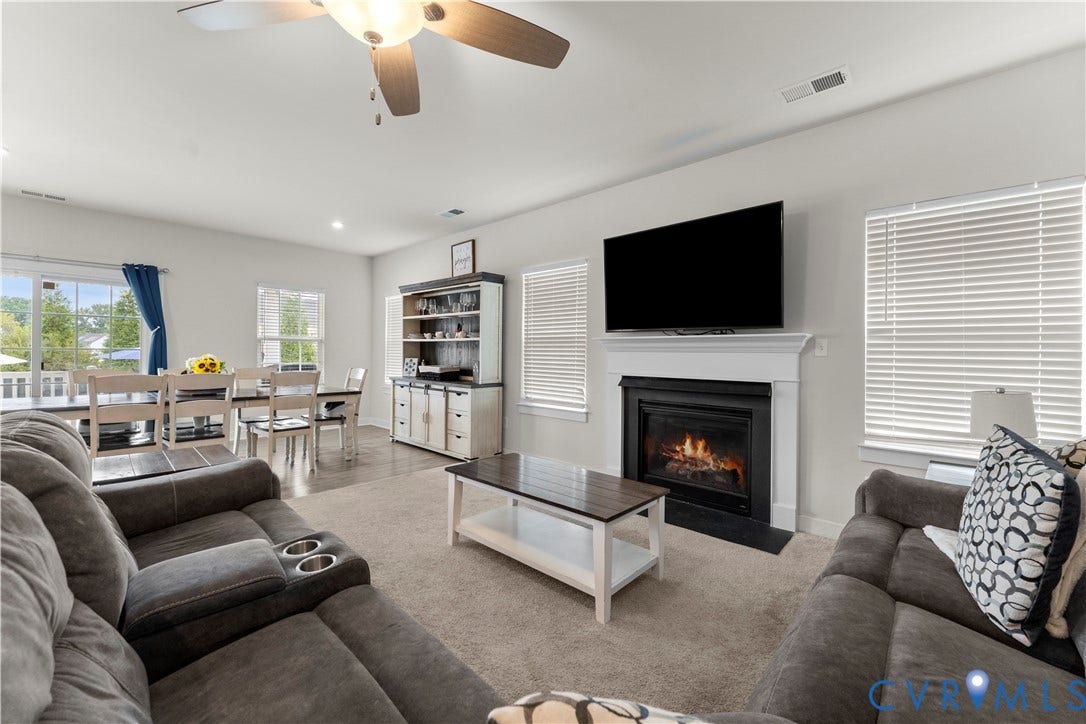 11707 Amara Drive, Chester / Highlands Golf Club, Chesterfield, VA 23838 Open-concept living space featuring a fireplace with a white mantel, ceiling fan, carpeted and wood-finish flooring, and white window blinds