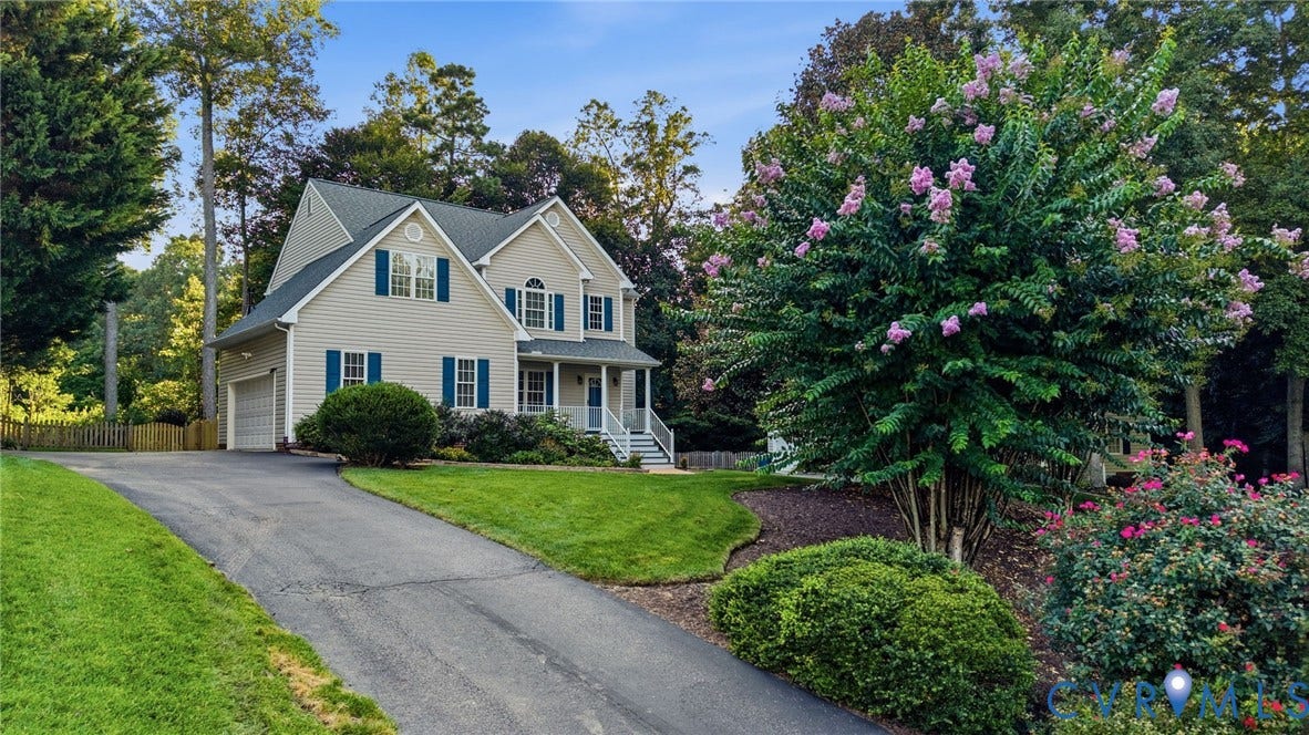 Two-story residence with a covered porch, attached garage, paved driveway, and established landscaping