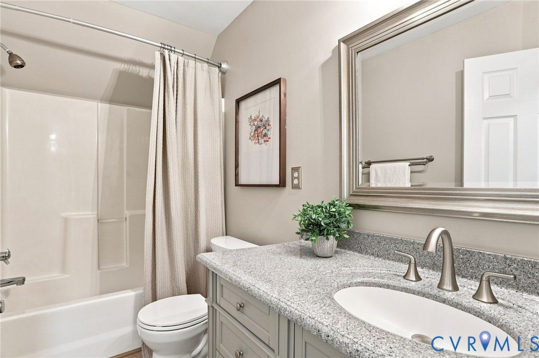 White shower-tub combination, vanity with light gray cabinetry, integrated sink, and granite-style countertop, brushed nickel faucet