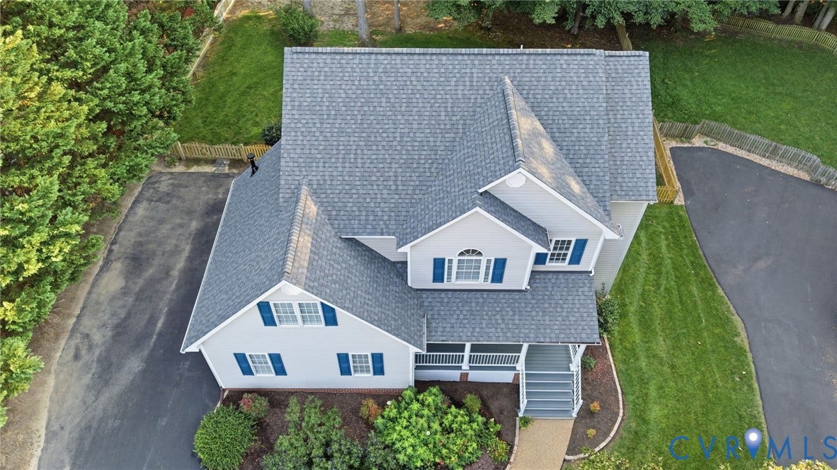 Light gray siding with blue window shutters, gray shingled roof, front porch with columns, and a paved driveway