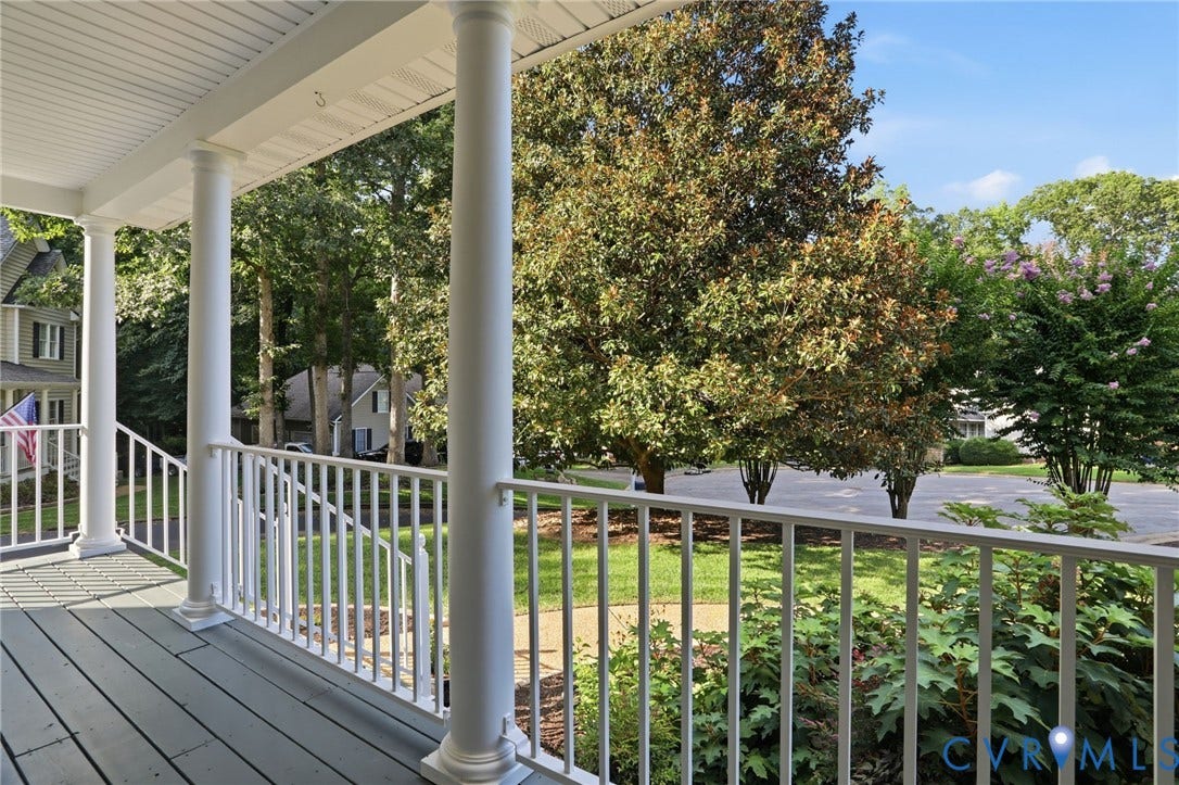 Expansive front porch featuring white columns and railing, with wood-finish decking and a beadboard ceiling
