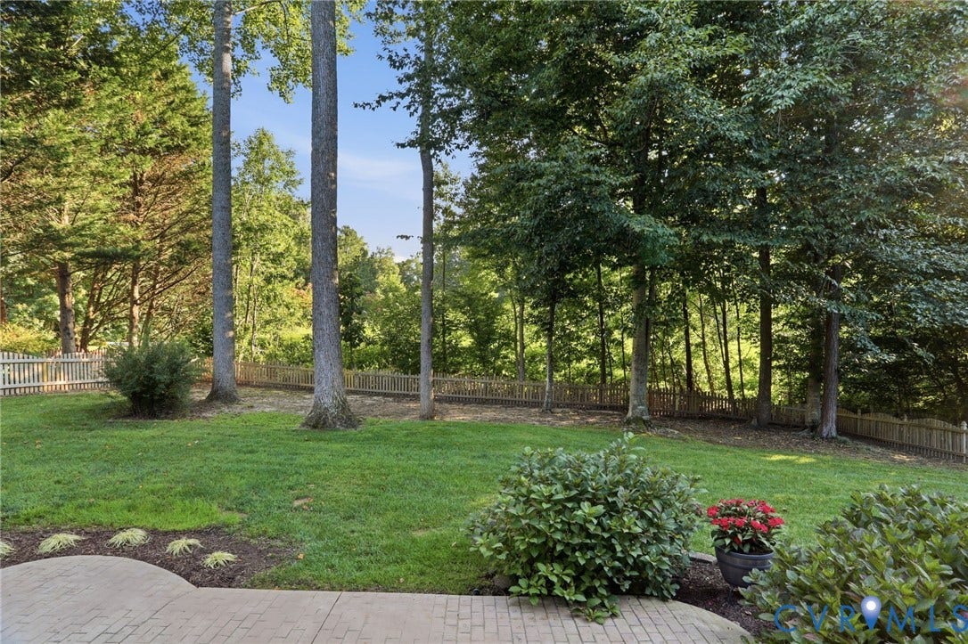 Expansive backyard featuring a manicured lawn, mature trees, and a decorative picket fence
