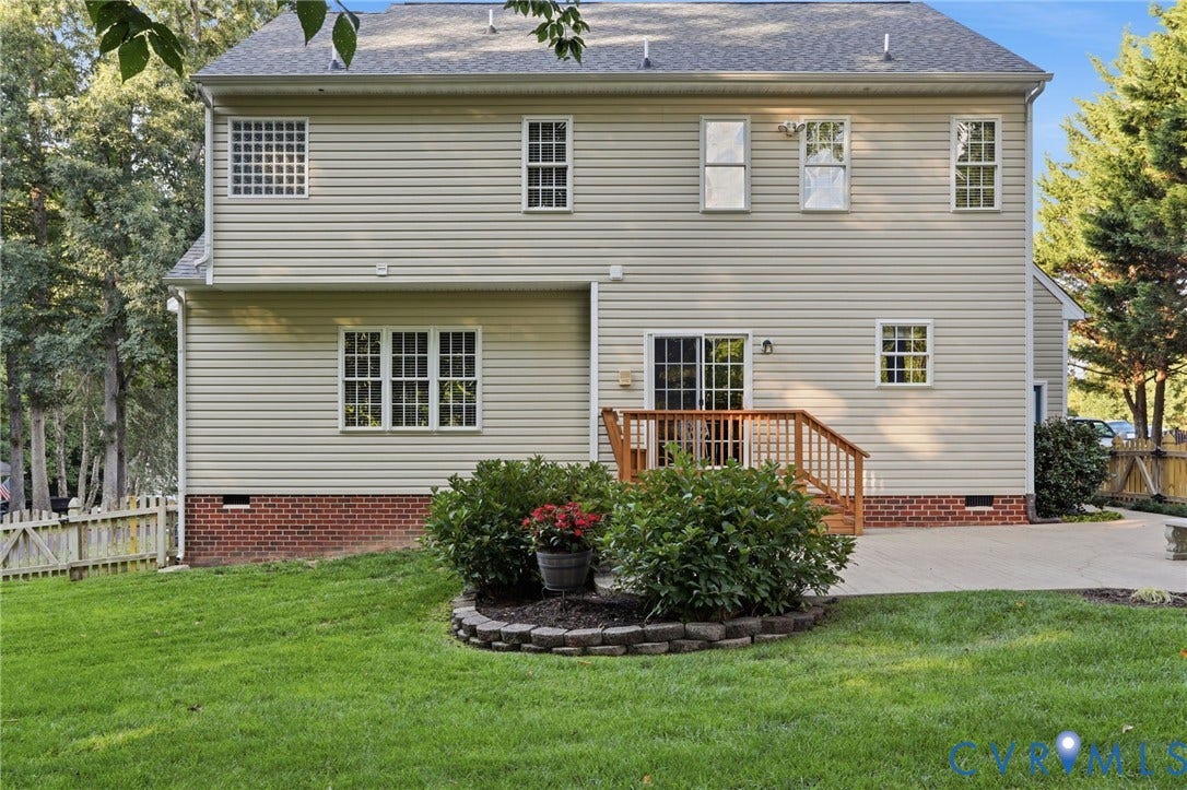 Rear exterior featuring beige siding, brick foundation, multiple windows, a wooden deck with railing, and a sliding glass door