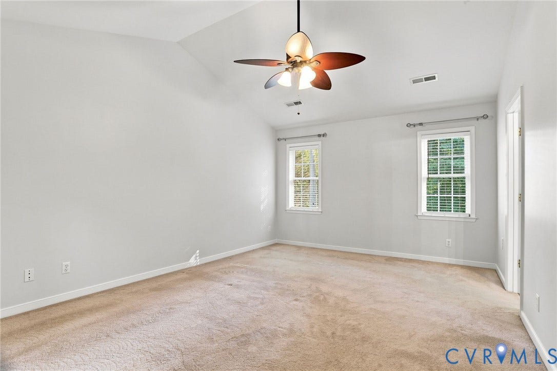 Vaulted ceiling, ceiling fan with integrated lighting, two windows with blinds, light-colored carpeting, neutral wall finishes