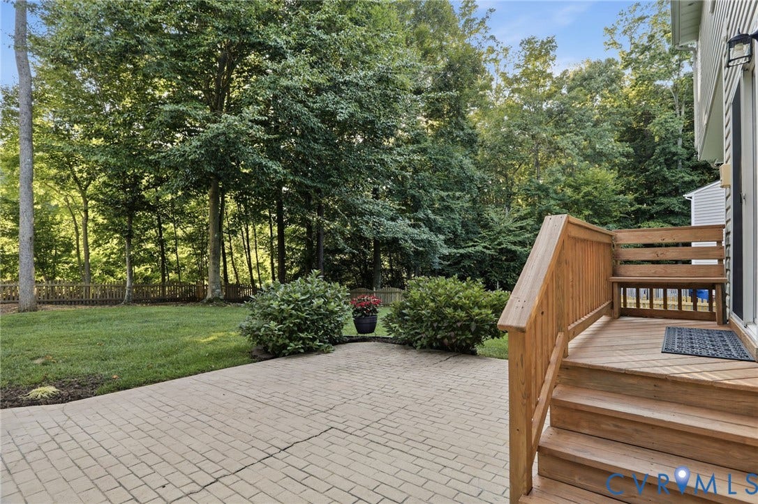 Expansive paved patio with a wood deck, wood railing, and a built-in wood bench