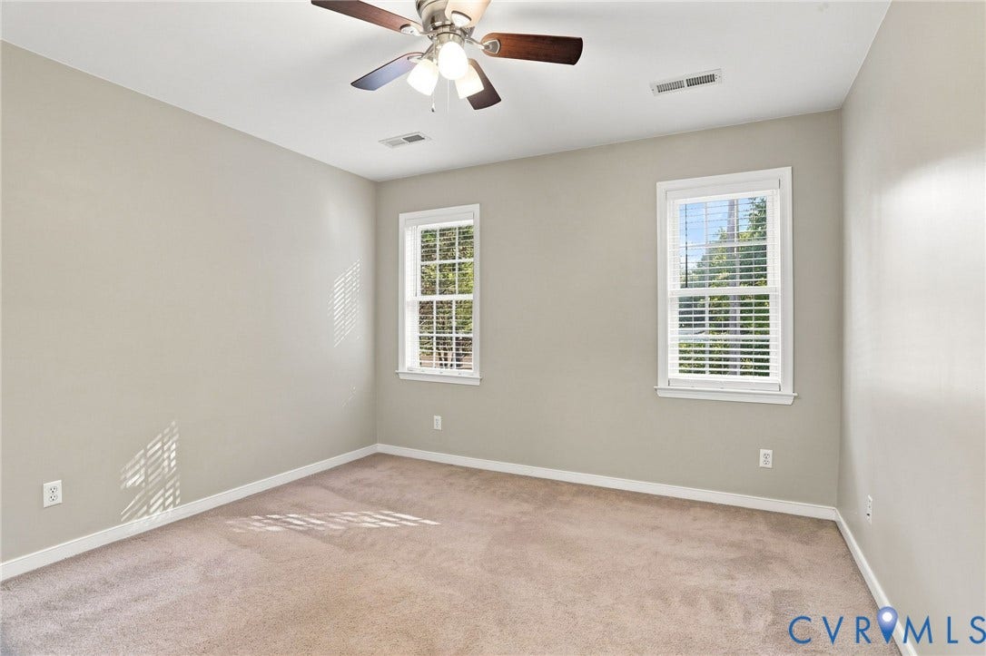 Neutral-toned walls, two windows with white blinds, and a ceiling fan with integrated lighting