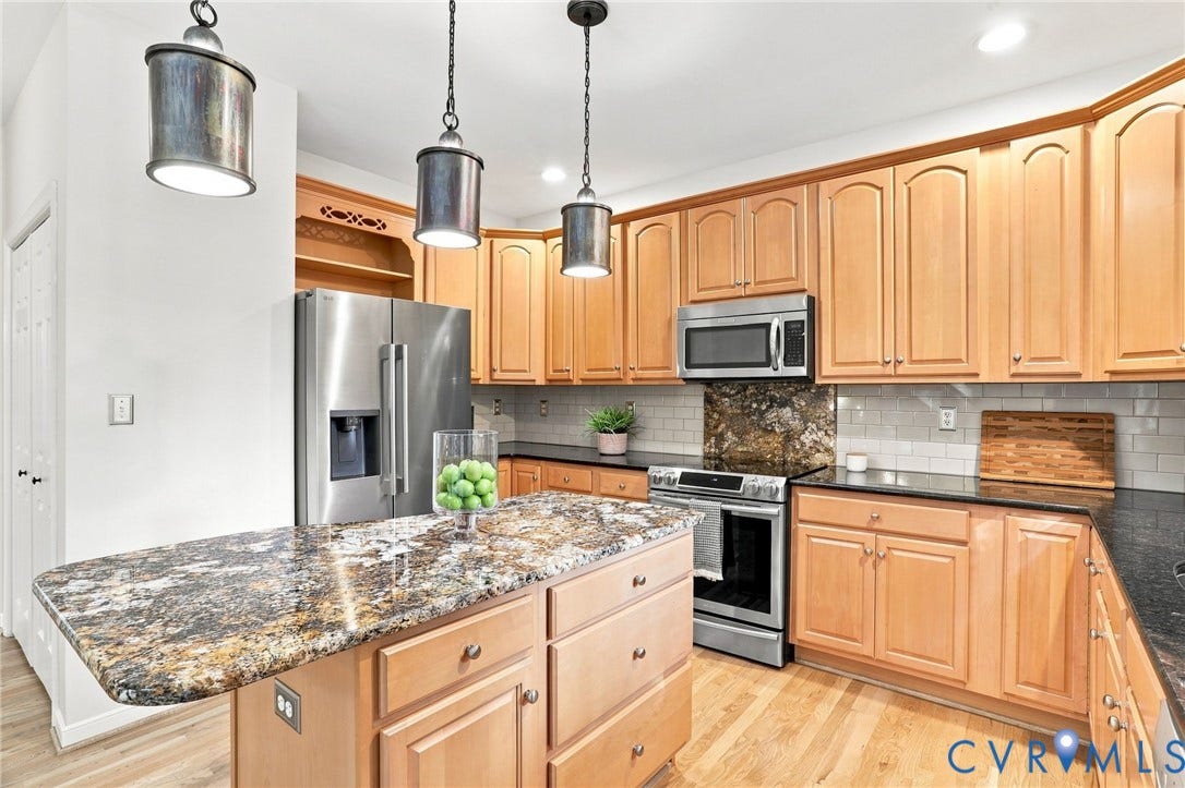 Stainless steel appliances, light wood-finish cabinetry, a multi-tone granite island, light subway tile backsplash, and dark countertops