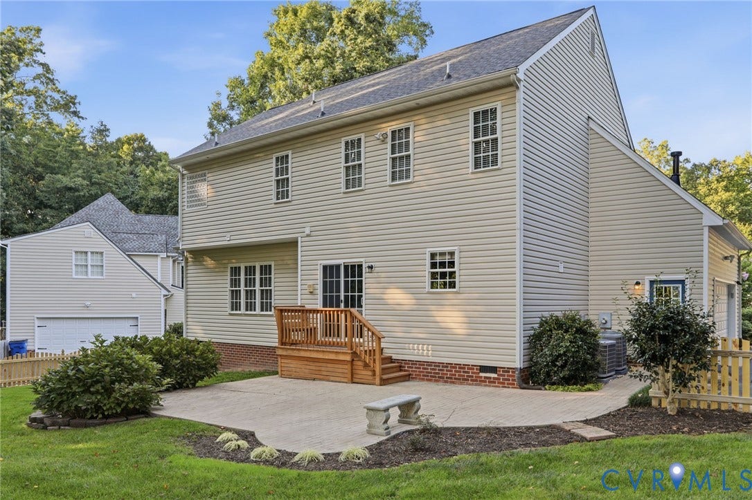 Exterior featuring light-colored siding, multiple windows, a wooden deck with railing, and a concrete patio