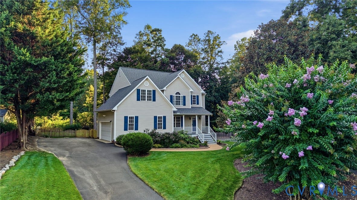 Siding exterior with blue shutters, a front porch with white railings, an attached garage, a paved driveway, and established landscaping
