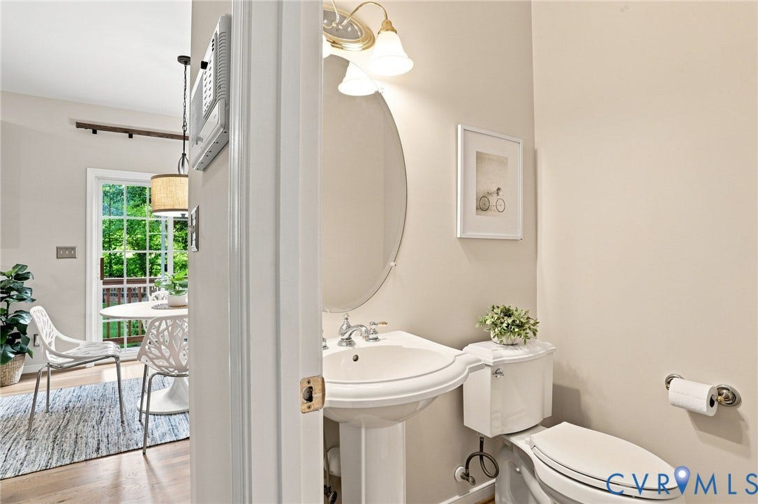 Pedestal sink with chrome fixtures and an oval mirror, porcelain toilet, and a transom window above the patio door