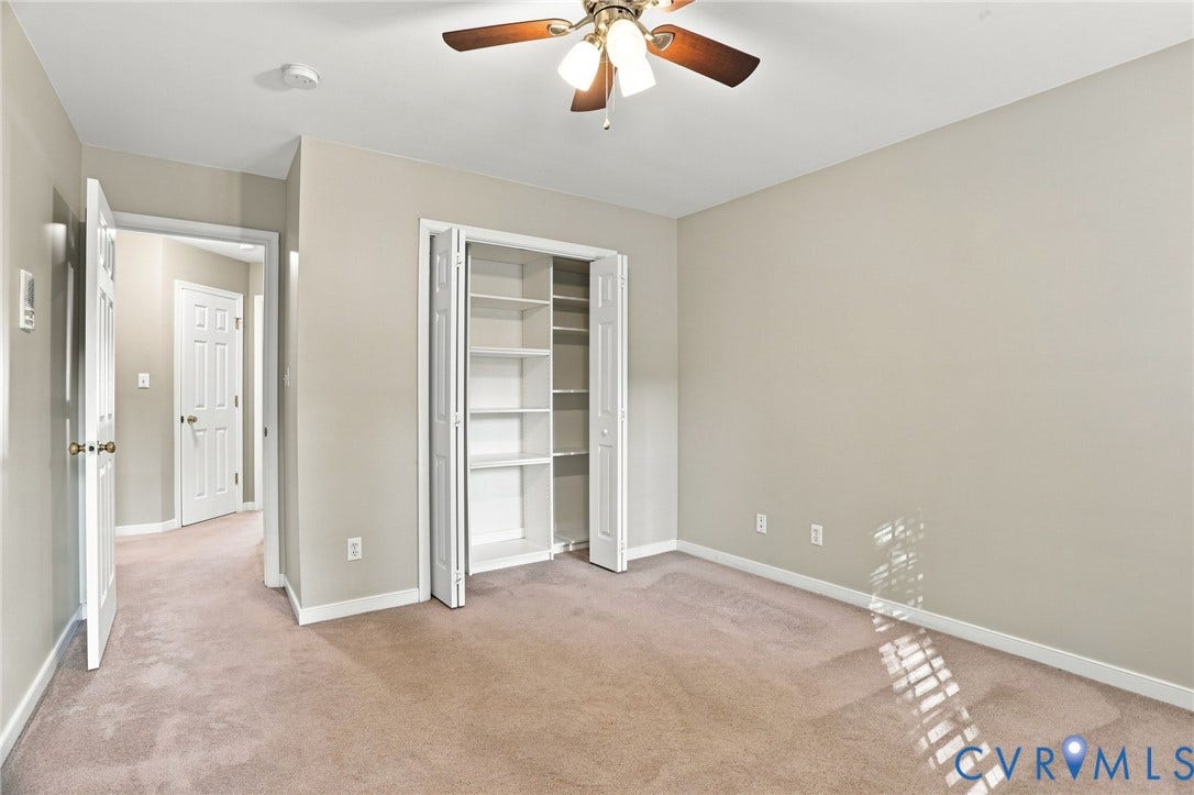 Neutral-toned walls, carpeted flooring, bi-fold closet doors with shelving, and a ceiling fan with light fixture