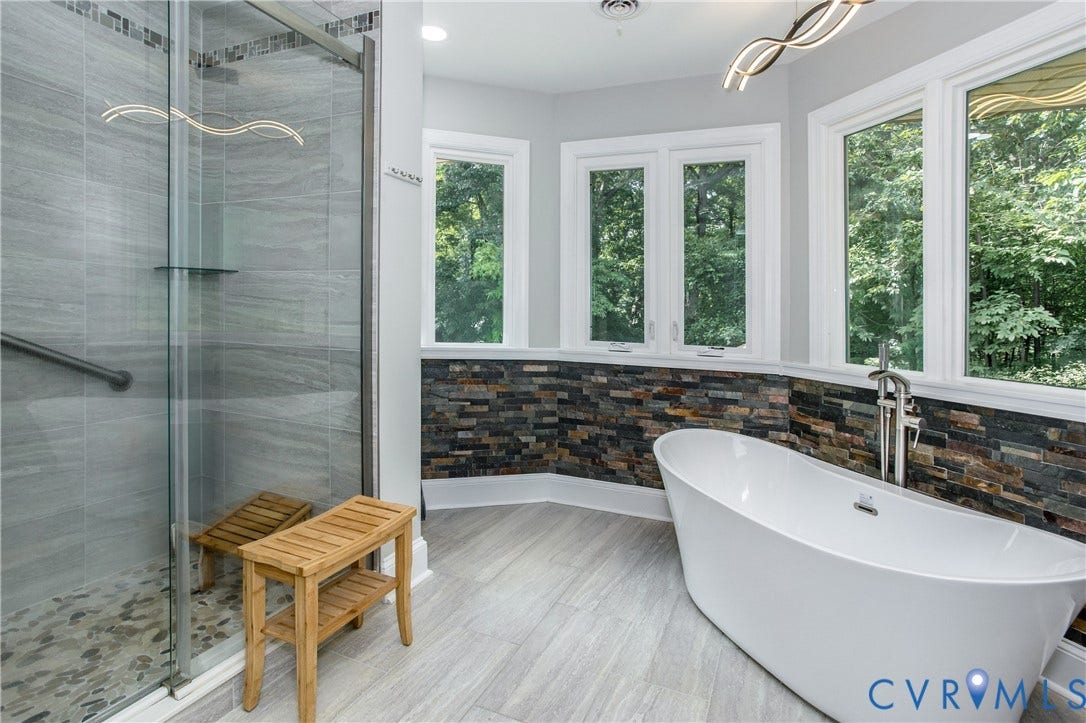 14530 Fox Knoll Drive, South Chesterfield, VA 23834 Walk-in shower with river rock base, freestanding soaking tub, stacked stone accent wall, and multiple windows