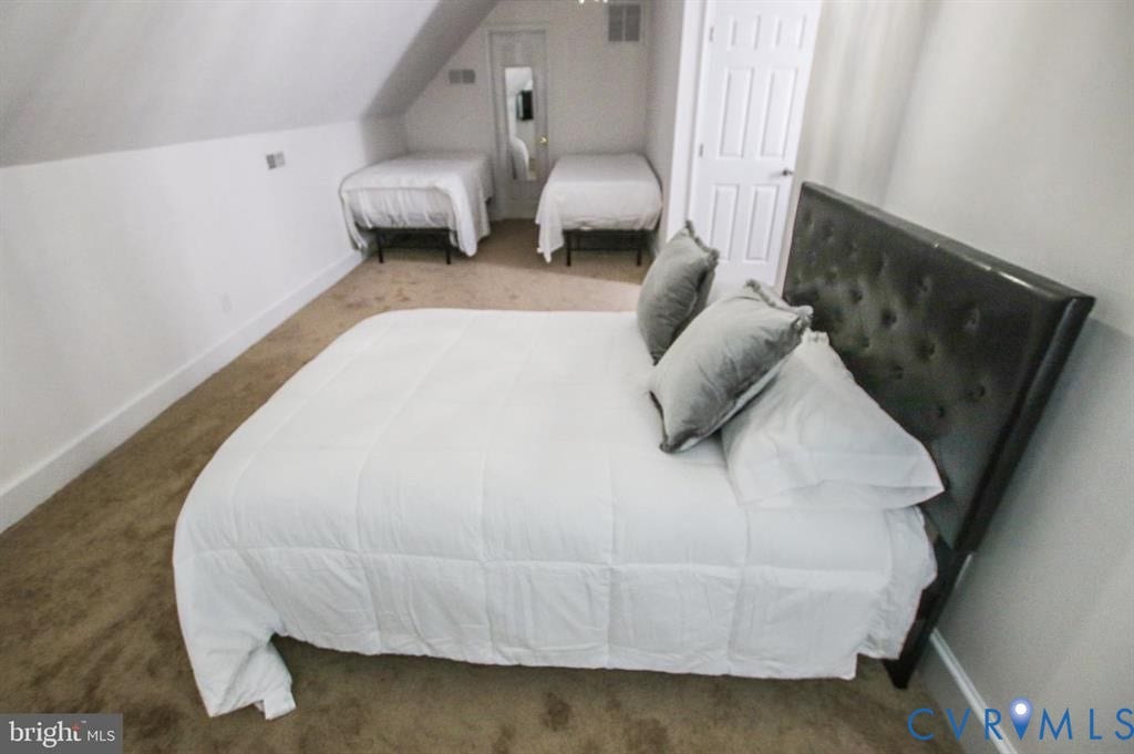 1910 W Main Street, The Historic Fan District, Richmond, VA 23220 Carpeted room with a tufted upholstered headboard, white walls, and an angled ceiling
