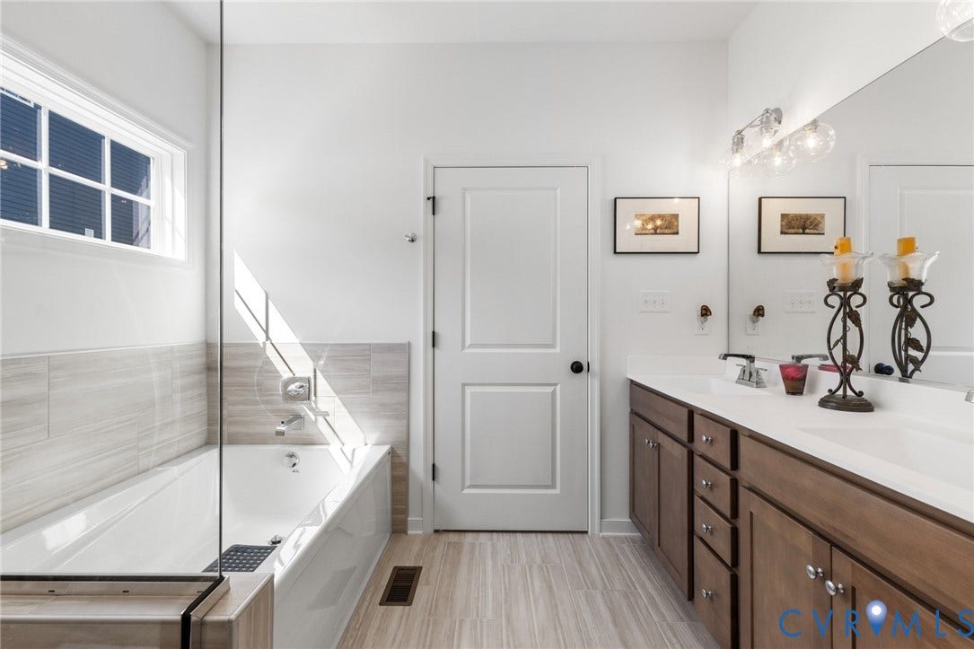 12906 Craftsbury Court, Midlothian, VA 23112 Light wood-finish flooring, a double vanity with brown cabinetry, white countertops, a large mirror, and a built-in bathtub with a window