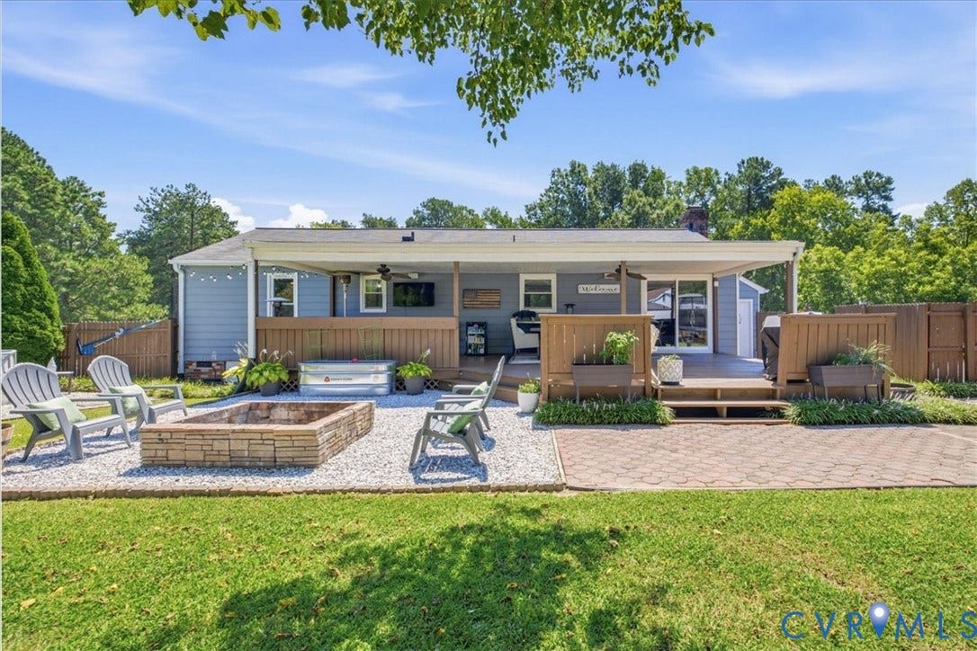 7900 Valencia Road, Chesterfield, VA 23832 Expansive backyard featuring a manicured lawn, a stone-clad fire pit, and a spacious wooden deck with a covered patio