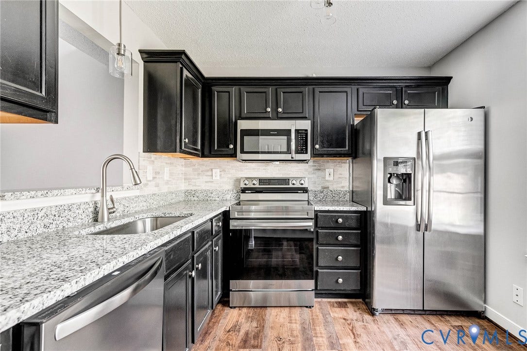 Kitchen featuring stainless steel appliances, dark wood cabinetry, granite countertops, tile backsplash, and wood-finish flooring