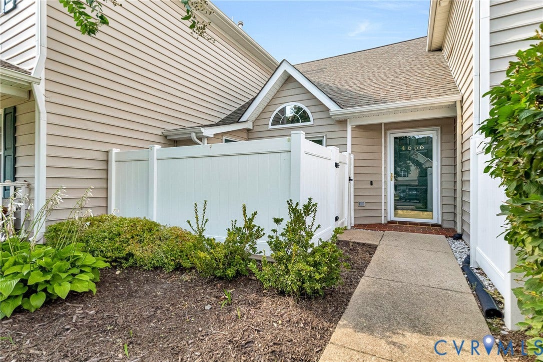 Entryway featuring a white privacy fence, an arched transom window, a clear glass storm door, and a concrete walkway