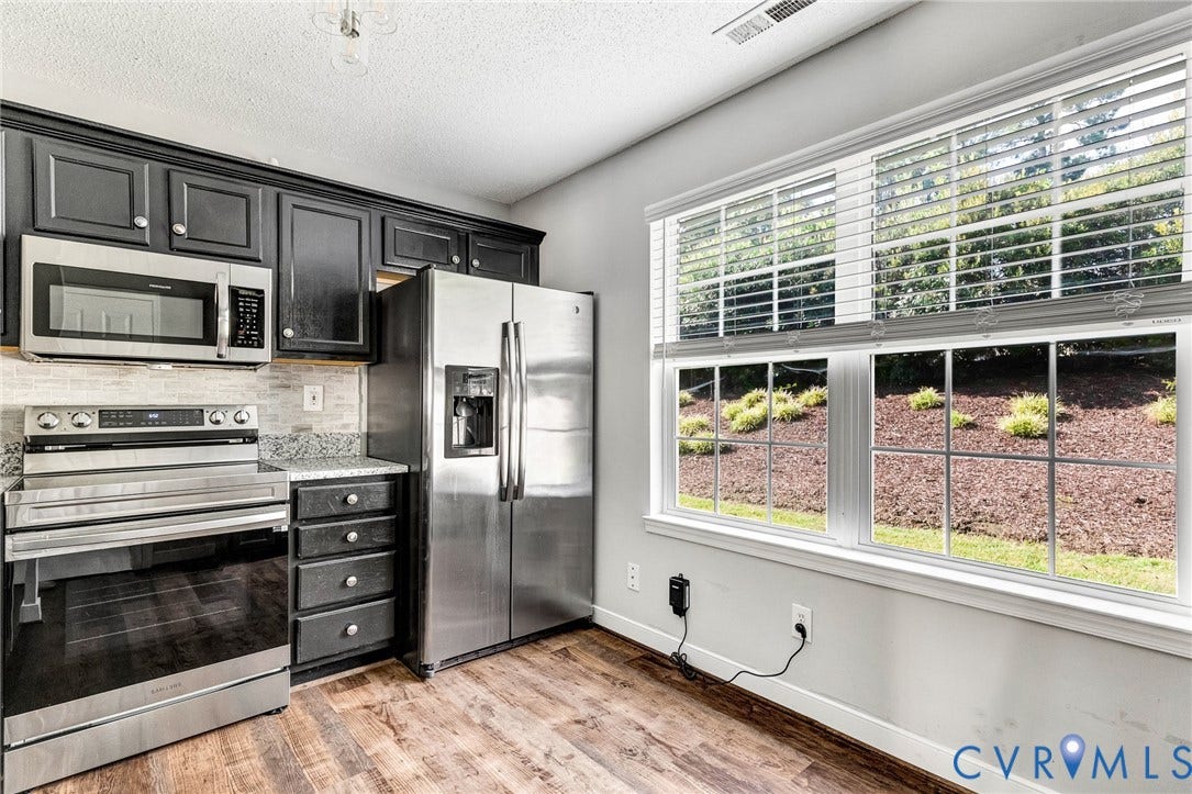 Kitchen featuring dark-finish cabinetry, stainless steel appliances, speckled countertops, tile backsplash, and wood-finish flooring