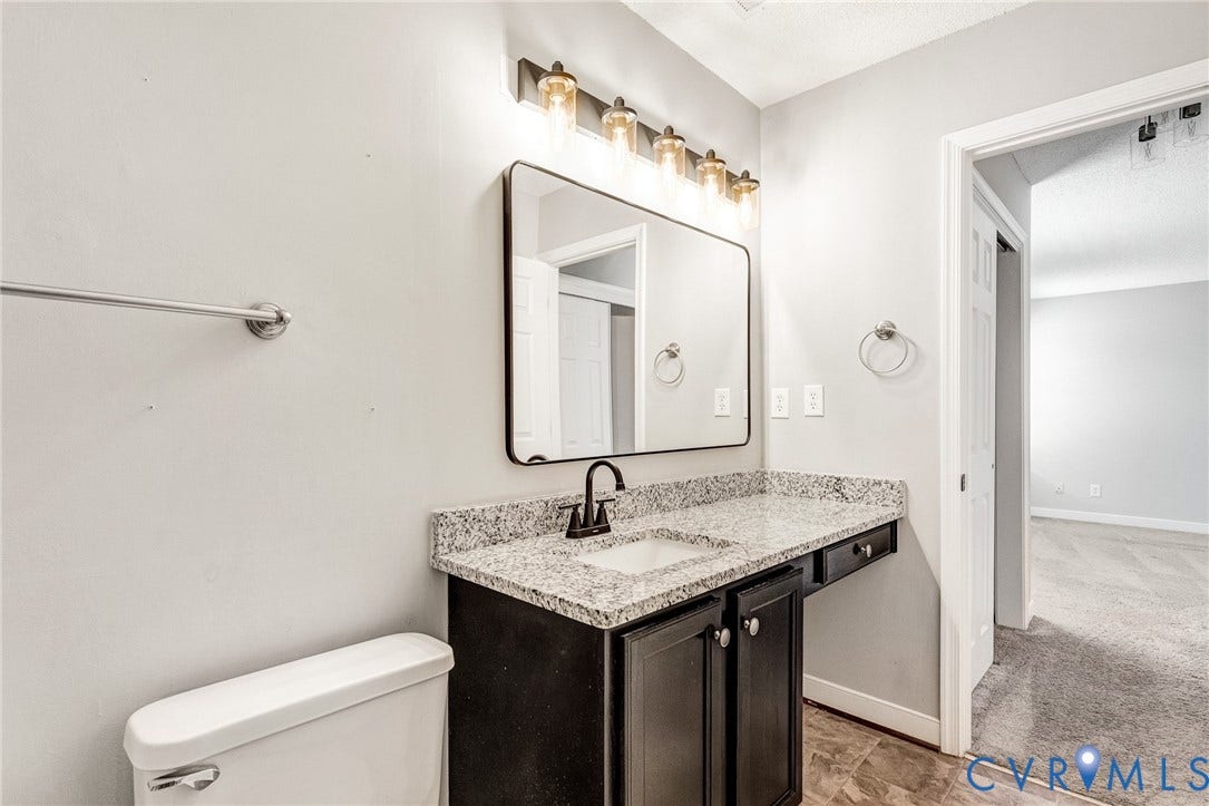 Granite-style countertop, dark wood-finish vanity, modern light fixture, rectangular framed mirror, and a contemporary black faucet
