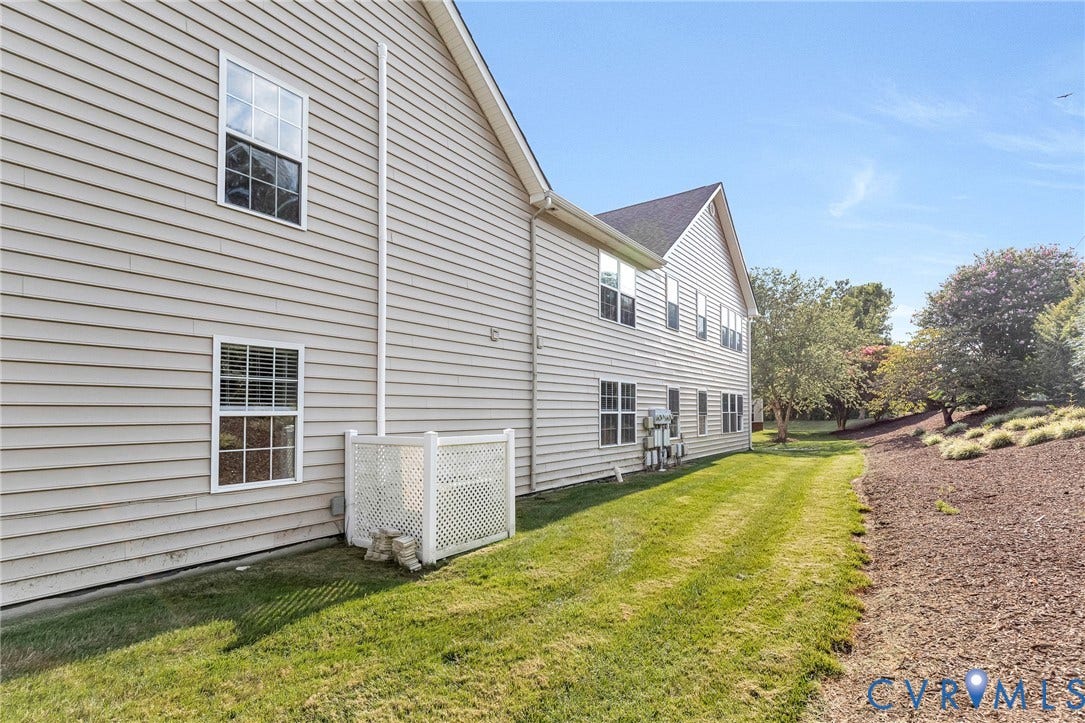 Siding exterior with multiple windows, pitched roofline, and a landscaped berm with mature trees
